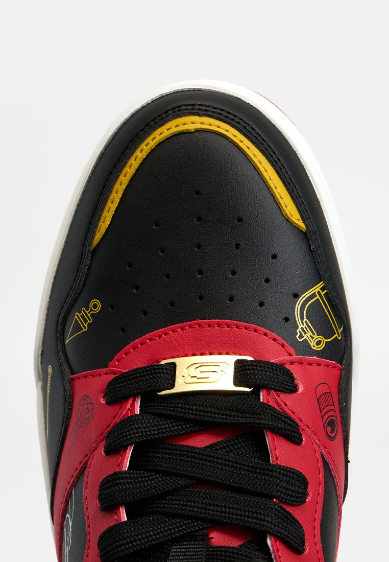 Zapatillas de cuero negras y rojas con acentos amarillos, que presentan una puntera perforada, cordones negros y una etiqueta con logo dorado en la lengua.