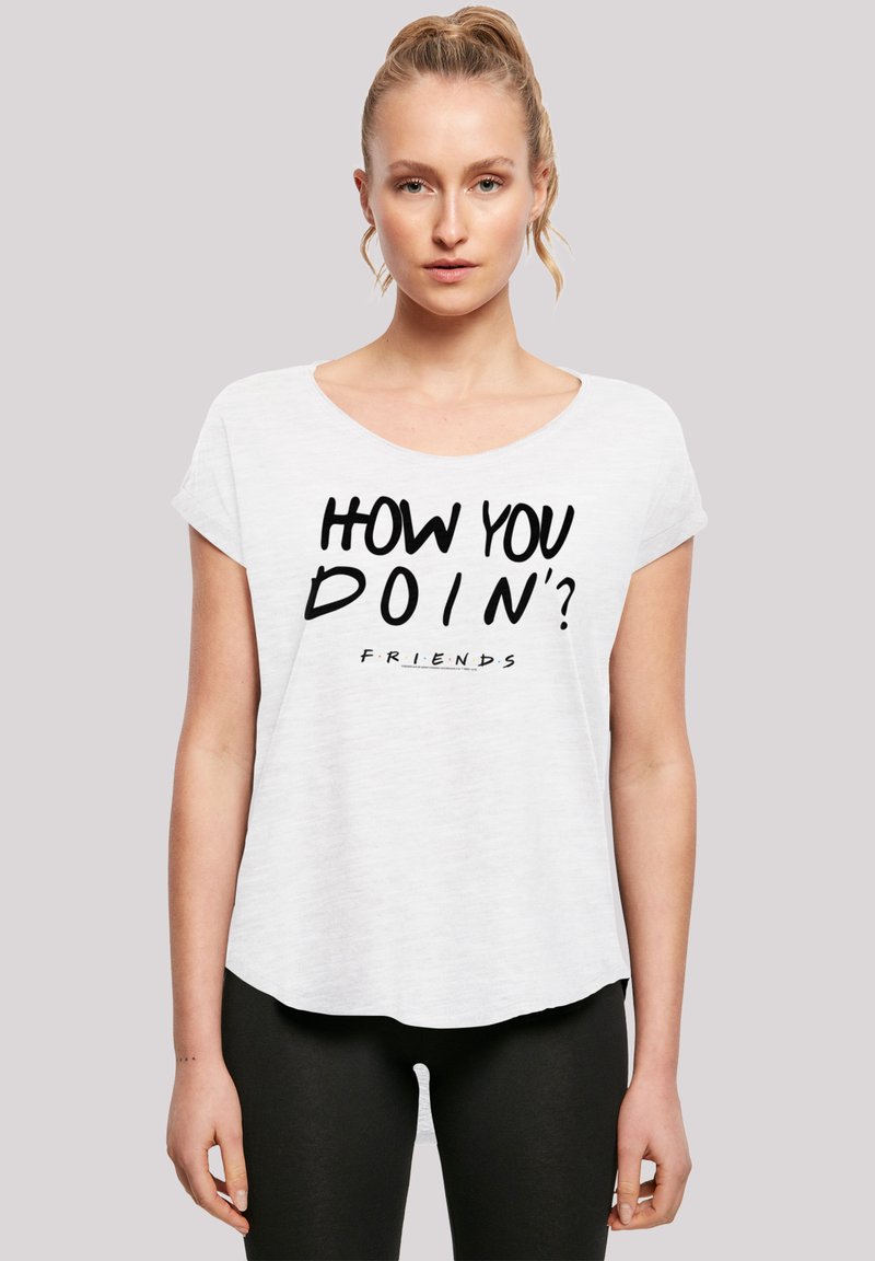 Hvit t-skjorte med korte ermer og rund hals. Har en svart grafisk tekst "HOW YOU DOIN'?" og "FRIENDS"-logo sentrert på forsiden.