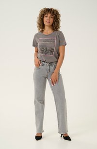 Camiseta gráfica gris con diseño de "Flores Silvestres de California" en rosa. Combinada con jeans rectos gris claro y tacones negros de punta. 