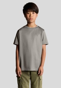 Grå bomulds t-shirt med korte ærmer og rund halsudskæring, prydet med et lille sort logo på brystet. Båret med olivengrønne cargo-bukser.