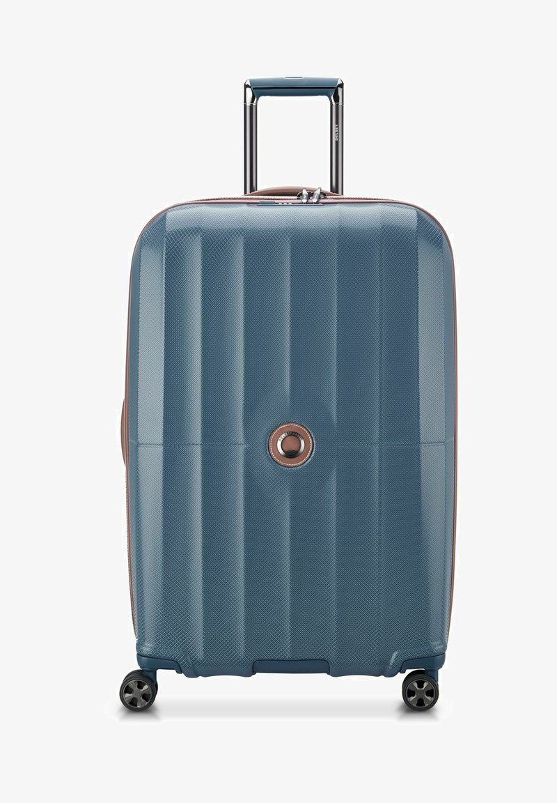 Valigia rigida di colore blu scuro con superficie testurizzata, caratterizzata da scanalature orizzontali, manico estraibile e quattro ruote per la mobilità.