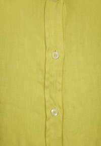 Camisa de lino amarilla con un acabado texturizado, que presenta una botonera frontal y botones redondos blancos.