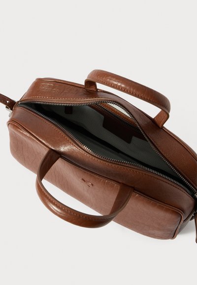 Barna bőr táska sima textúrával, nyitott cipzárral, két fogóval és csíkos szövetbélés belül.