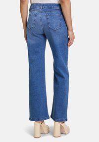 Hellblaue, weit geschnittene Jeans aus Denim mit mittelhohem Bund, Gesäßtaschen und einem sauberen Saum. Kombiniert mit beigen Plateauschuhen.