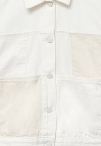 Biała denimowa koszula z zapięciem na guziki z przodu, wieloma kieszeniami o teksturowanym wykończeniu oraz subtelnymi detalami przeszycia. Gładkie wykończenie materiału.