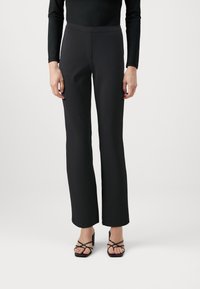 Pantaloni neri su misura con un design a gamba dritta, realizzati in un tessuto liscio; indossati con tacchi neri con fasce.