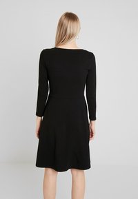 Svart långärmad klänning i mjukt tyg, med rund halsringning, figurnära överdel och utsvängd kjol. Ren design utan synliga mönster.