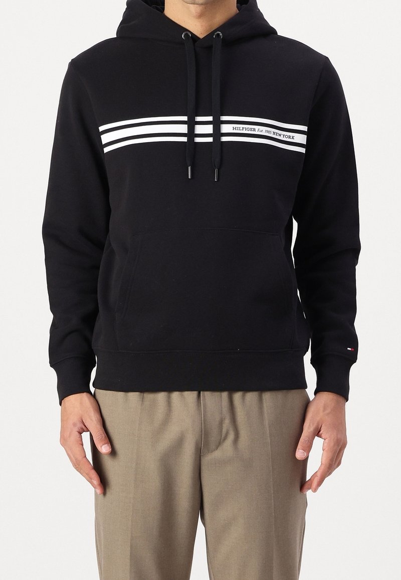 Sweat à capuche noir en matière polaire, avec une poche kangourou à l'avant, des rayures horizontales blanches et un logo sous les rayures.