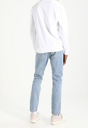 Weißes Langarmhemd, blaue Jeans, helle Sneakers mit pinken Akzenten. Fokus auf die Rückansicht; einfaches Design, weiche Stofftextur.