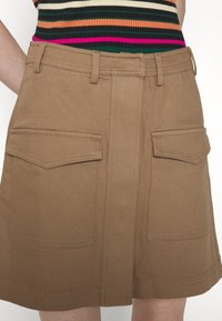 Jupe marron taille haute avec poches à rabat devant et passants pour ceinture, portée avec un top côtelé rayé multicolore.
