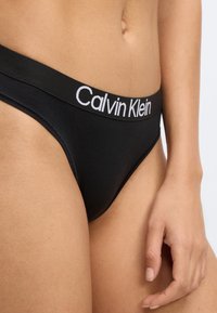 Μαύρο στρινγκ Calvin Klein με μαλακή ελαστική ζώνη μέσης που φέρει λευκό κείμενο λογοτύπου. Κατασκευασμένο από λείο ύφασμα, σχεδιασμένο για κομψή εφαρμογή.