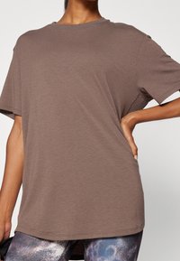 Camiseta oversized marrón con cuello redondo, mangas cortas y una textura suave, con un sutil patrón jaspeado.