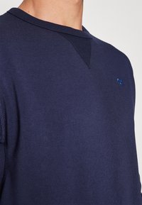 Σκούρο μπλε φούτερ με υφή, διαθέτει στρογγυλή λαιμόκοψη και μικρό μπλε λογότυπο στο στήθος, ορατές ραφές στα πλαϊνά.