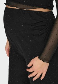 Czarny strój z tkaniny o fakturowanej powierzchni z małymi, błyszczącymi ozdobami. Góra posiada przezroczysty, falbaniasty dół; dopasowane, marszczone spodnie.