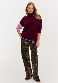 Burgundowy sweter z golfem z różowymi akcentami, zestawiony z spodniami w panterkę. Całość posiada niebieskie wykończenie i wyrazisty detal z metką.