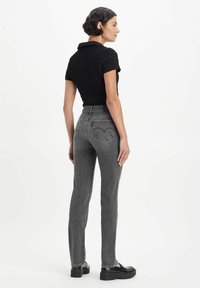 Black textured short-sleeve top paired with high-waisted, fitted gray jeans featuring two back pockets and visible stitching details. Black shoes.