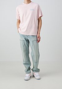 Camiseta de algodón rosa claro con un pequeño logo azul de Levi's, combinada con pantalones cargo de mezclilla de lavado claro y zapatillas blancas con acentos rosas.