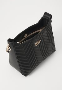 Sac à main noir matelassé avec texture en chevron, logo doré, fermeture zippée supérieure et bandoulière. Matériau lisse, forme structurée, design compact.