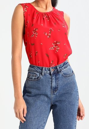 Top rosso senza maniche con motivo floreale, scollatura arricciata, abbinato a jeans in denim blu a vita alta. Texture del tessuto liscia.