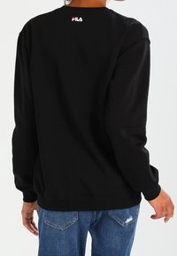 Sudadera negra de algodón con mangas largas, cuello redondo y dobladillo acanalado. Presenta un pequeño logo de FILA en rojo y blanco en la parte superior de la espalda.