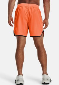 Orange sportshorts med dragsko i midjan, sidospjäll och svarta detaljer längs kanterna. Tillverkade av lätt och andningsbart material.