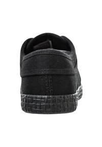 Zapatilla de tela negra con talón redondeado, que presenta una textura de suela de goma tejida negra y detalles cosidos a lo largo de los bordes.