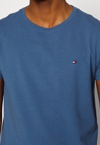 Cotton t-shirt in a dusk blue color with a round neck. Features a small embroidered logo in red, white, and blue on the left chest area.