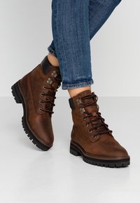 Botas de senderismo de cuero marrón con ojales metálicos y detalles en negro. La suela es robusta y texturizada, diseñada para proporcionar tracción y durabilidad.