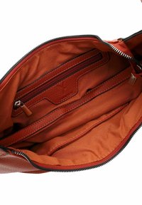 Red leather handbag interior featuring an orange fabric lining, multiple pockets, a zippered compartment, and signature branding detail.