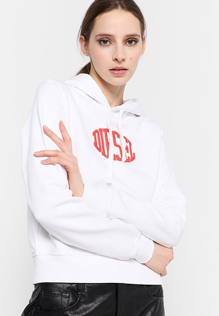 Hoodie blanc avec un logo "DIESEL" rouge, capuche avec cordon, poignets et ourlet côtelés. Le modèle pose les bras croisés devant un fond neutre.