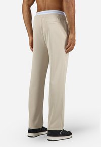 Beige joggebukser med hvit elastisk liv, med baklomme, glatt tekstur og avslappet passform, sammen med svarte joggesko.