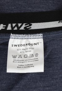 Etichetta in tessuto blu navy con la scritta "SWEDEMOUNT," che indica il 60% di lana Merino e il 40% di Tencel. Istruzioni per la cura e simboli di lavaggio stampati in bianco e nero.