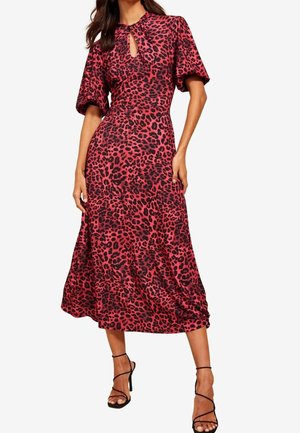 Donna che indossa un vestito midi rosso e nero con stampa leopardata, maniche a sbuffo, scollo a goccia anteriore e tacchi alti neri con cinturini.