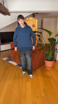 Mörkblå huva med framficka, kombinerad med svarta cargobyxor och silverfärgade sneakers. Inomhusmiljö med växter och möbler.