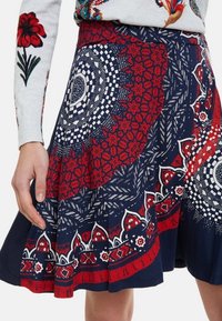 Blå kjol med intrikata röda och vita blommönster samt geometriska mönster, med en utsvängd design och en texturerad midjeband.