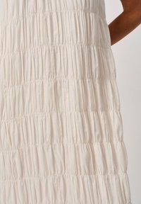 Hellbeiges Kleid mit geraffter Textur und horizontalen Raffungslinien, gefertigt aus einem weichen Stoff, der leicht fällt.