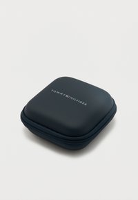 Μικρή τετράγωνη θήκη σκούρου μπλε χρώματος με φερμουάρ, στρογγυλεμένες άκρες και το λογότυπο Tommy Hilfiger στο πάνω μέρος, τοποθετημένη σε λευκό φόντο.