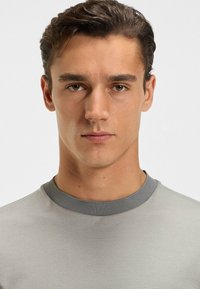 Graues, strukturiertes Kurzarmhemd mit einem kontrastierenden dunkelgrauen Kragen, das einen figurschmeichelnden Schnitt und einen glatten Stoff aufweist.