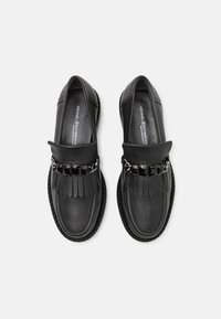 Juodos odinės slip-on tipo bateliai su fransuoto priekiu, papuošti grandinėle, su tekstūruota padu ir lygia apdaila.