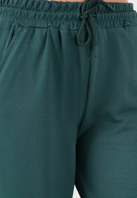 Pantaloni jogger leggeri e verdi con vita elastica e cordoncino. Texture liscia, tasche laterali e vestibilità rilassata.