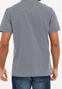 Chemise à manches courtes en noir et blanc avec un motif en losange, dotée d'un col classique et d'un ourlet droit, vue de dos.