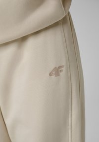 Pantalon en tissu beige doux avec couture latérale cousue et petit logo "4F" sur la cuisse supérieure.