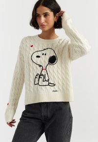 Cremfarbener Kabelstrickpullover mit einem schwarzen und roten gestickten Snoopy-Design. Rippbündchen an den Ärmeln und am Saum; lockere Passform.