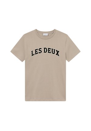 Μπεζ βαμβακερό T-shirt με καμπύλο μαύρο λογότυπο "LES DEUX" στο στήθος. Κοντά μανίκια και κλασική στρογγυλή λαγουδέρα.