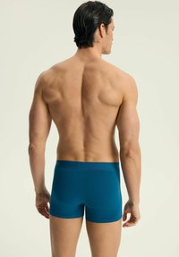 Miękkie, turkusowe boxerki o dopasowanym kroju, średniej wysokości pasie, o gładkiej fakturze, pokazane z tyłu.