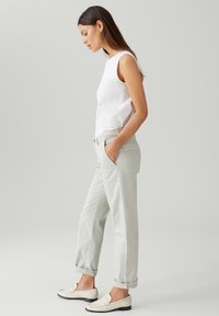 Top bianco senza maniche, pantaloni grigi chiari a vestibilità morbida con tasche, orli risvoltati e mocassini bianchi; design minimalista e texture morbida.
