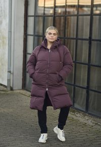 Dlhý, nadýchaný kabát v tmavofialovej farbe so zipsom a kapucňou. Obsahuje veľké prešívané sekcie. Nosený na čiernych nohaviciach a bielych teniskách.