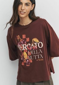 Brown cotton t-shirt with loose fit, featuring a colorful fruit-themed graphic text reading "Mercato della Frutta" and short sleeves.