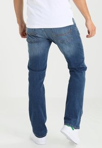 Blå denimjeans med rak passform, med bakfickor och subtila blekta områden. Bärs med vita sneakers.