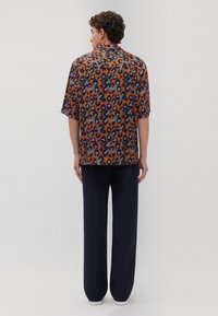 Camicetta marrone a maniche corte con un design leopardato blu e nero, abbinata a pantaloni larghi blu navy. Vestibilità rilassata con un colletto.